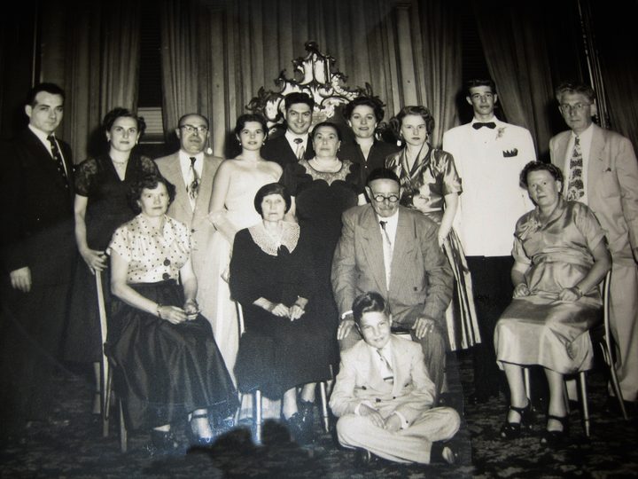 At a family wedding. Myrna’s mother is seated far left, and younger brother Dan sits cross-legged on the floor. In the back row, Sam is second from left and their father third from right, with Myrna to his left.